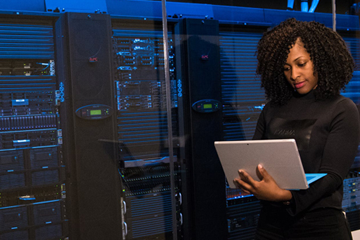 Woman on computer standing next to large computer servers