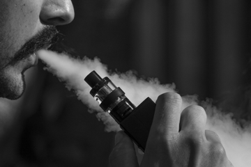 Image of man with moustache blowing vapour out of his mouth whilst holding a vape pen